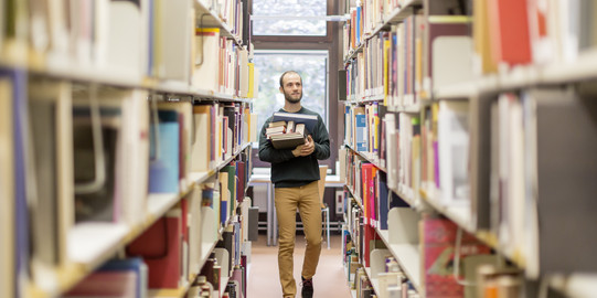 Ein Mann läuft mit Büchern in der Hand durch die Bibliothek