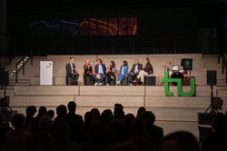 Foto: Mehrere Personen sitzen auf einer Bühne bei einer Podiumsdiskussion.