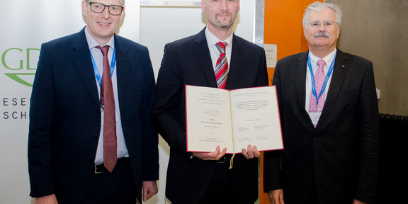 Verleihung Innovationspreis 2019 Dr. Franz von Nussbaum, Dr. Andreas Brunschweiger und Prof. Dr. Stefan Laufer stehen in einer Reihe und lächeln in die Kamera. Dr. Brunschweiger hält eine Urkunde in der Hand.