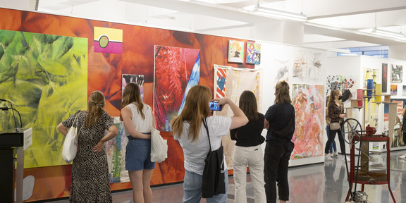 Mehrere Personen schauen sich ein großes rotes Bild einer Kunstausstellung an.