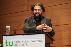 Das Foto zeigt Prof. Aladin El-Mafaalani an einem Rednerpult auf dem vorne das TU-Logo sowie die Aufschrift "Technische Universität Dortmund" zu lesen ist. Im Hintergrund befindet sich eine Holzvertäfelung.