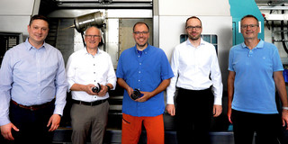 Foto: Fünf Personen stehen vor einer großen Maschine in einer Werkhalle.