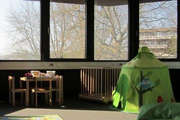 Eltern-Kind-Raum mit Spielzelt und Tunnel in grün und einem Kindertisch und Laufstall im Hintergrund