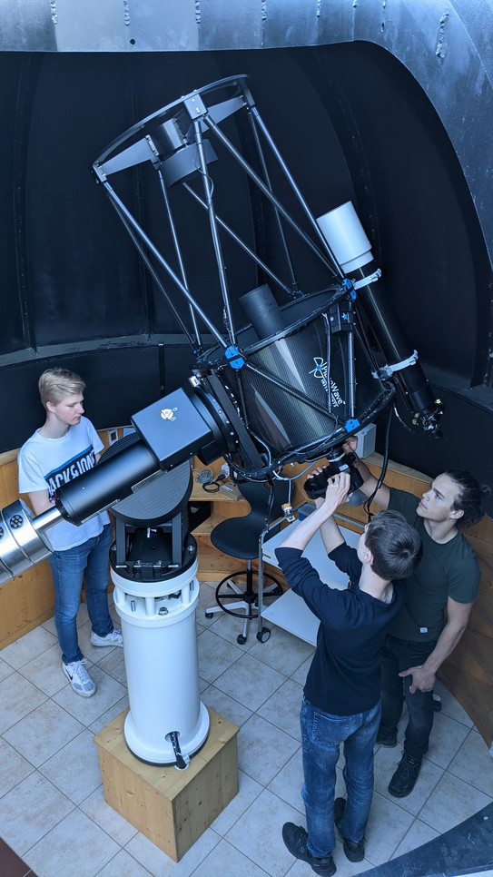 Mehrere Schüler stehen um ein Teleskop in einer Sternwarte. 