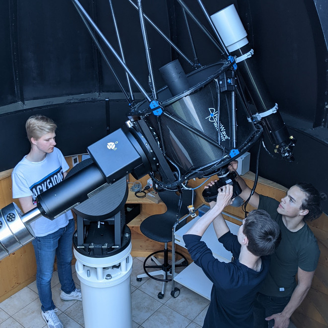 Several students standing around a telescope in an observatory.