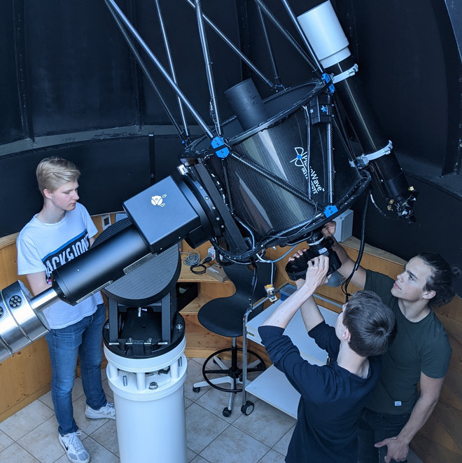Mehrere Schüler stehen um ein Teleskop in einer Sternwarte. 
