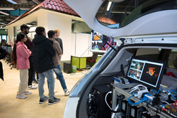 Auf dem Foto ist rechts im Bild ein offener Autokofferraum, indem sich Technik und ein Bildschirm befindet. In der linken Seite des Fotos ist eine kleine Gruppe zu sehen, die sich etwas auf einem Bildschirm anschaut.