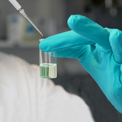 Hand in Laborhandschuh im Anschnitt, mit einer Pipette wird Lösungsmittel in ein keines Reagenzglas gegeben
