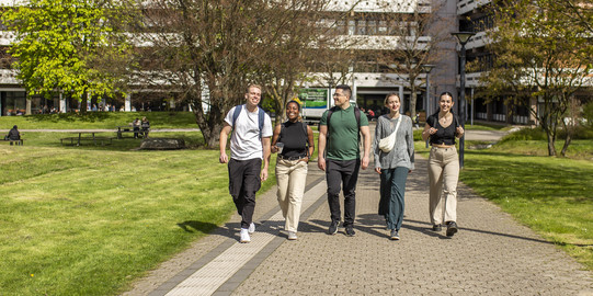 Foto: Fünf Studierende spazieren über den sonnigen Campus der TU Dortmund.