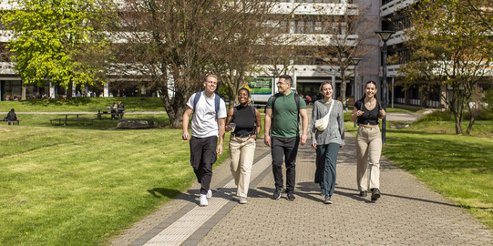 Foto: Fünf Studierende spazieren über den sonnigen Campus der TU Dortmund.