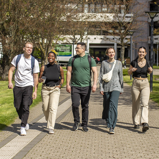 Foto: Fünf Studierende spazieren über den sonnigen Campus der TU Dortmund.