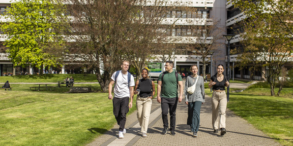Foto: Fünf Studierende spazieren über den sonnigen Campus der TU Dortmund.