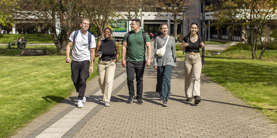 Foto: Fünf Studierende spazieren über den sonnigen Campus der TU Dortmund.