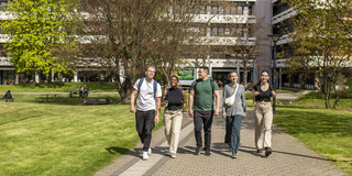 Foto: Fünf Studierende spazieren über den sonnigen Campus der TU Dortmund.