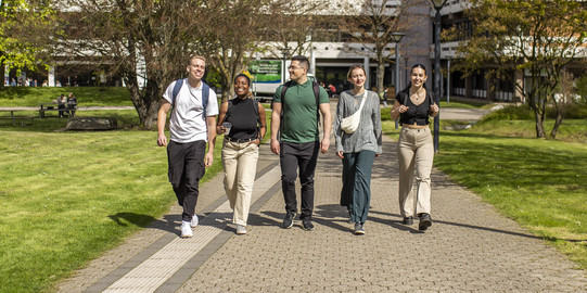 Photo: Five students stroll across the sunny campus of TU Dortmund University.
