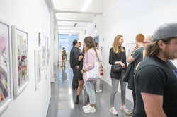 Rundgang Kunst Konversationen In einem Gang stehen Menschen in Grüppchen, betrachten die Kunstwerke an den Wänden und unterhalten sich.