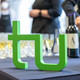 Ein grünes TU-Logo steht auf einem Tisch vor einer Reihe von gefüllten Sektgläsern.