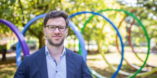 Foto: Ein Porträt von Prof. Igor Schapiro, einem brünetten Mann mit blauem Blazer, auf dem sonnigen Campus der TU Dortmund.