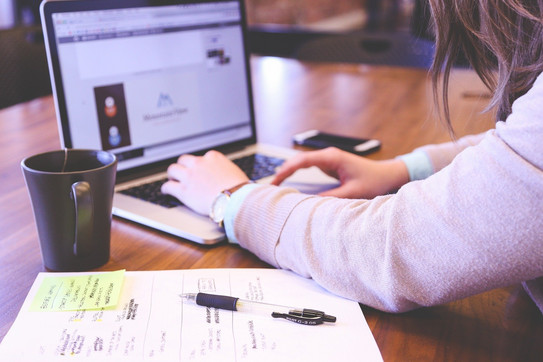 A woman is writing on her laptop. There are notes next to it.