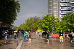 Foto: Menschen stehen auf einem Campusplatz, während im Hintergrund ein Regenbogen zu sehen ist.