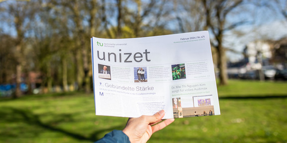 A hand is holding the current issue of the campus newspaper unizet up in the air.