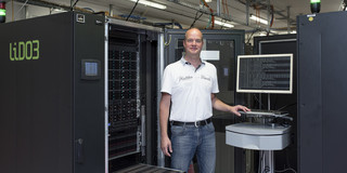A man in jeans and a white T-shirt stands in front of a man-sized black computer with the inscription "lido3".
