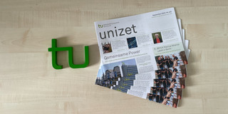 Mehrere unizet-Zeitungen liegen neben einem TU-Logo auf einem Tisch