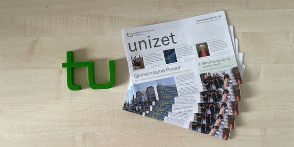 Mehrere unizet-Zeitungen liegen neben einem TU-Logo auf einem Tisch