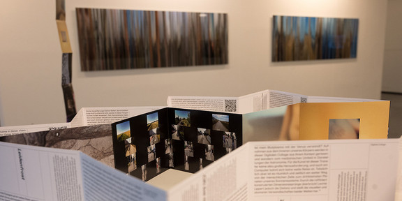 Ausstellung Physik und Kunst Im Hintergrund hängen Kunstwerke an einer Wand, im Vordergrund befindet sich das Endlosleporellos.