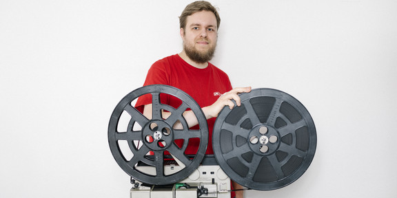 Portrait of Stefan Kunzmann next to an old film projector.