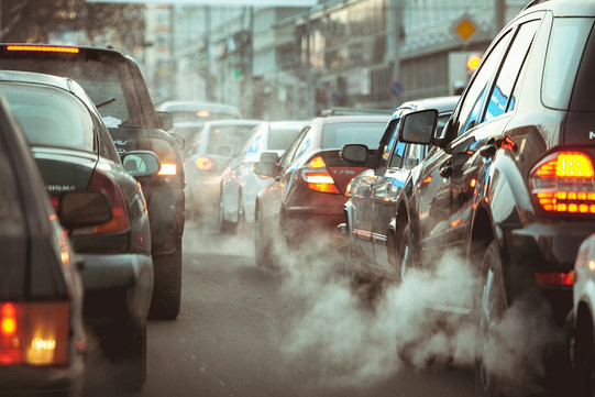 Mehrere Autos stehen in einer Schlange hintereinander auf der Straße und es steigt weißer Rauch auf.