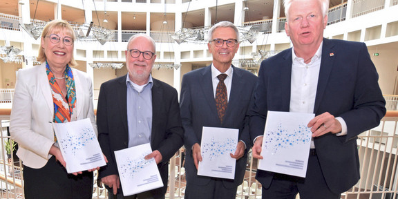 Evaluationsbericht Masterplan Eine Frau und drei Männer halten jeweils den Bericht in Händen