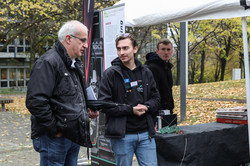 Two men are talking and standing in front of a TU Dortmund booth.