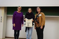 Eine Teilnehmerin der SchülerUni hält einen Beutel hoch und 2 Frauen lächeln neben ihr in die Kamera. 