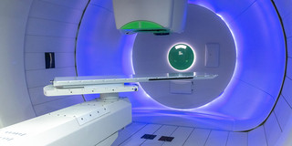 Modern treatment room for proton therapy with blue lighting and medical equipment.