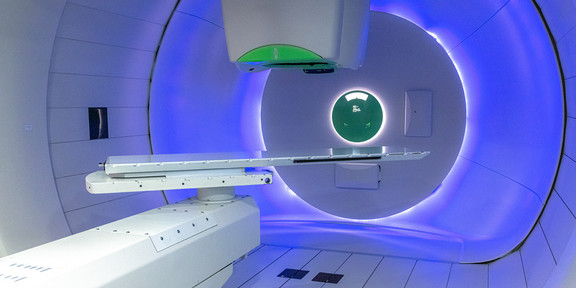 Modern treatment room for proton therapy with blue lighting and medical equipment.