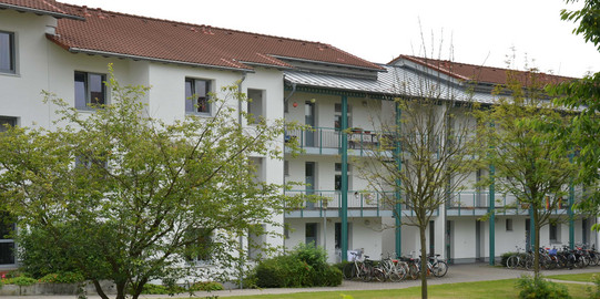 Wohnheim EF Dreigeschossige Wohnanlage mit rotem Dach, davor stehen Bäume auf einer Wiese