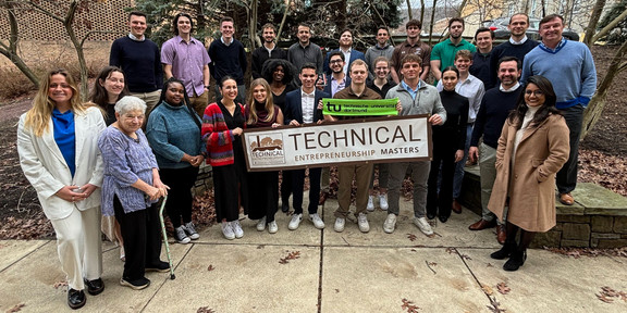 Zu sehen sind alle Teilnehmenden der Technical Entrepreneurship Week auf einem Gruppenfoto. Einige Studierende halten ein Banner mit der Aufschrift "Technical Entrepreneurship masters". Ein weiterer Student hält einen grünen Schal mit der Aufschrift "Technische Universität Dortmund".