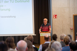 Das Bild zeigt TU-Rektor Bayer hinter einem Rednerpult, im vorderen Teil des Bildes ist das Publikum von hinten zu sehen.