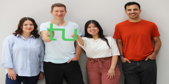 Vier Studenten halten TU Logo hoch