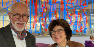 Foto: Prof. Weiler und Prof. Havenith-Newen lächeln mit Kafeetassen in der Hand in die Kamera.