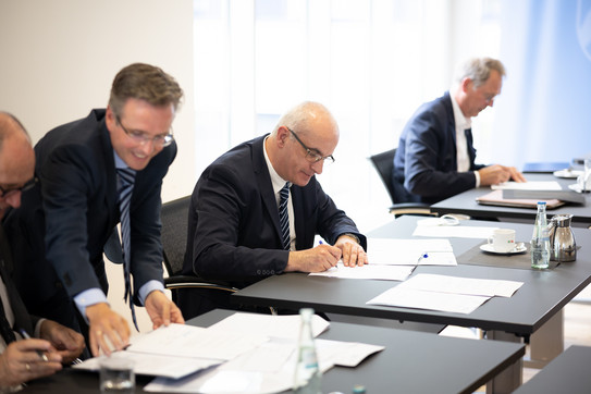 Signing of the cooperation agreement Three men in suits sign documents.