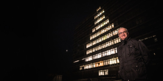 Weihnachtsgruß Rektor Manfred Bayer steht vor dem zehnstöckigen Mathetower, dessen Fenster so beleuchtet sind, dass die Silhouette eines Weihnachtsbaums zu erkennen ist.