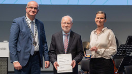 Dezember Das Bild zeigt Bayer, Müller-Böling, Flatten, welche nebeneinanderstehend in die Kamera lächeln. Müller-Böling hält eine Urkunde für eine weitere Universitätsmedaille in seinen Händen.