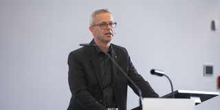 TU Chancellor Markus Neuhaus, a man with short gray hair and glasses, stands at a lectern in the lecture hall and gives a lecture.