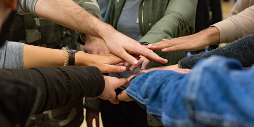 A circle of people holding their hands into the middle of the circle