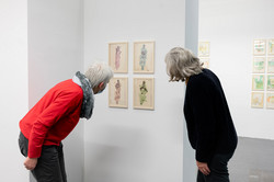 Ausstellung Goldenes Wunder Zwei Frauen begutachten vier an der Wand hängende Bilder.