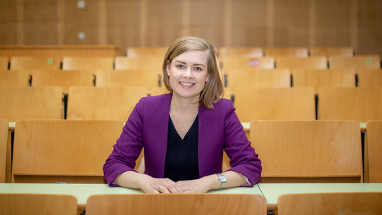 A woman (Dr. Carolin Funke) sits in a row of tables in a lecture hall and poses for the photo.