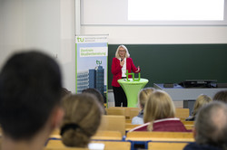 Frau Melle steht mit Mikrofon neben einem TU-Banner. Im Vordergrund sind Hinterköpfe zu sehen.