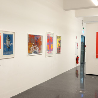 Vier Künstlerplakate hängen an einer weißen Wand.